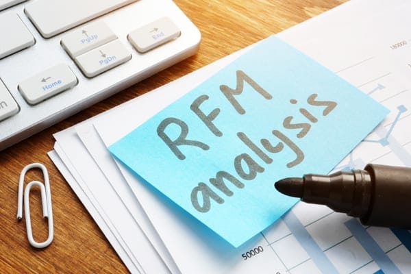 Keyboard paper clip stack of papers a marker and a sticky note stating RFM Anaysis