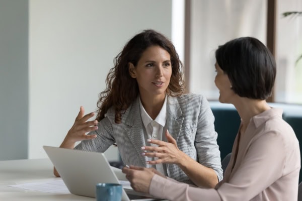 coach speaking to client and showing them something on a laptop while client speaks using her hands