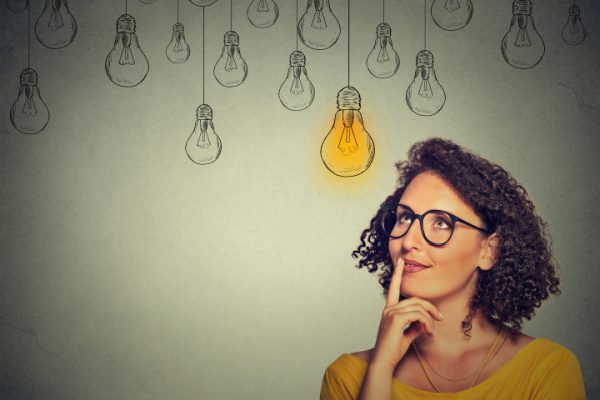 woman looking at light light bulb drawing hanging above her head with other unlit light bulb drawings also hanging